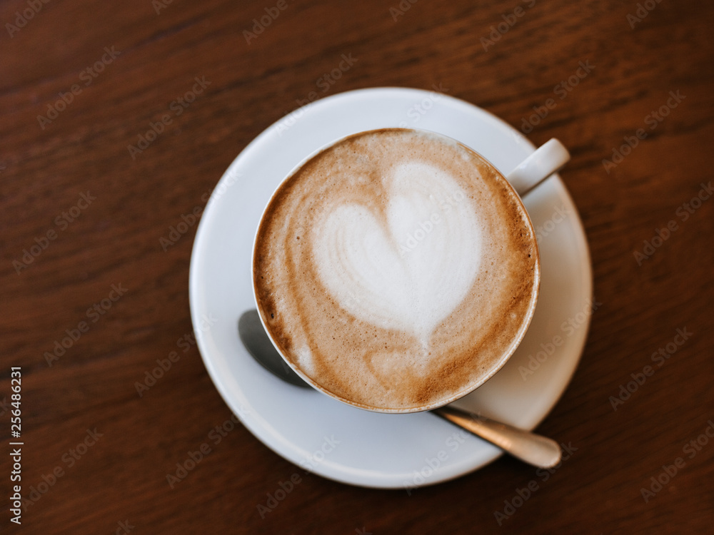 One cup of cappuccino with latte art on wooden table, white ceramic cup, yop view. Cafe culture. One cup of cappuccino with latte art on wooden table, white ceramic cup, yop view. Cafe culture.