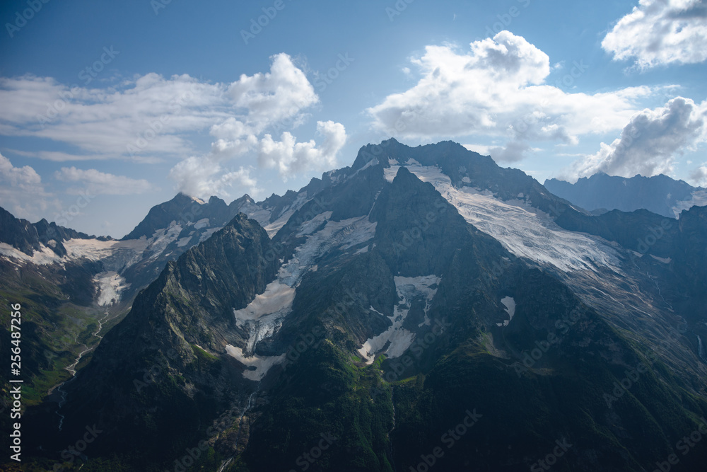 The peaks of the Caucasus Mountains in cloudy clouds and the rays of the sun through them in the outskirts of Dombai. And on the tops of snow lies. The peaks of the Caucasus Mountains in cloudy clouds and the rays of the sun through them in the outskirts of Dombai. And on the tops of snow lies.