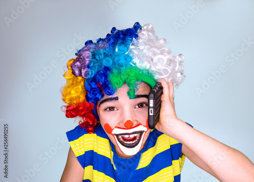 Portrait of happy funny clown kid holding smartphone and enjoying good news. Positive and expression concept. Isolated on gray.pantomimic expression. emotions. April Fool's Day, April 1
