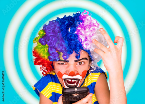 Portrait of clown kid holding smartphone and angry because of bad news.A boy screaming while talking on the phone. Negative and expression concept.pantomimic.emotions. April Fool s Day  April 1