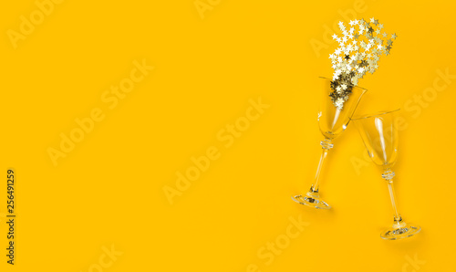 Golden confetti in the shape of stars fly out of champagne glasses on yellow background Flat lay Top view. Creative composition, concept of firework, holiday, party, birthday, christmas or new year