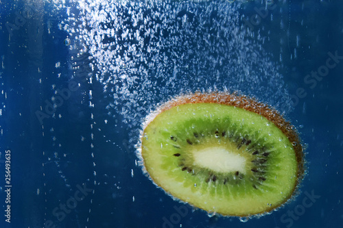 fresh piece of kiwi falling into the water on a blue background texture closeup macro