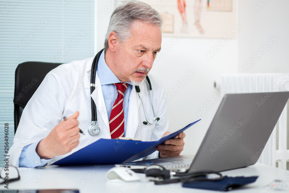 Senior doctor working at his laptop in his studio Senior doctor working at his laptop in his studio
