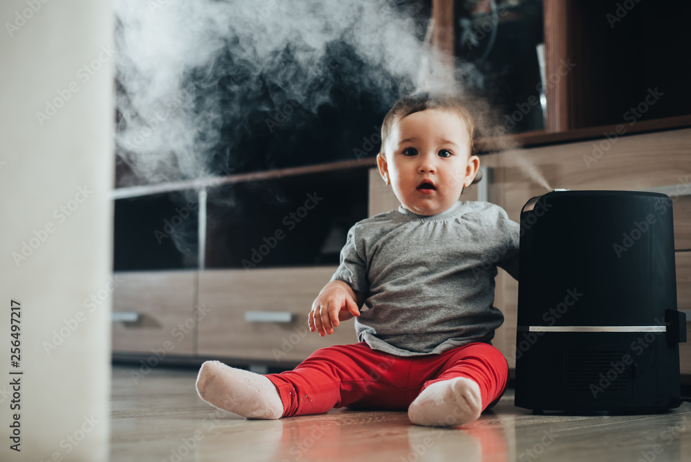 a little girl in red pants looks and touches the humidifier. Moisture in the house concept a little girl in red pants looks and touches the humidifier. Moisture in the house concept
