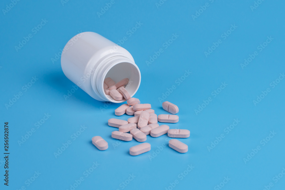 Pink pills, tablets and white bottle on blue background.