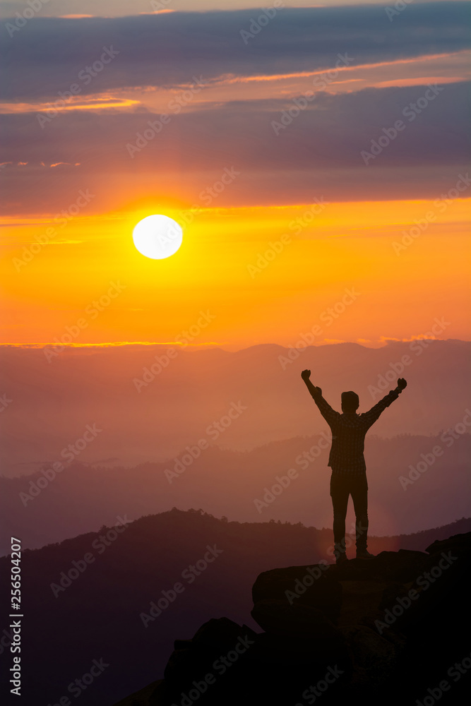Men raise their arms in sunrise,Landscape with silhouette of a standing happy man with backpack and raised-up arms on the mountain peak on the background of cloudy sky at colorful sunset in summer.