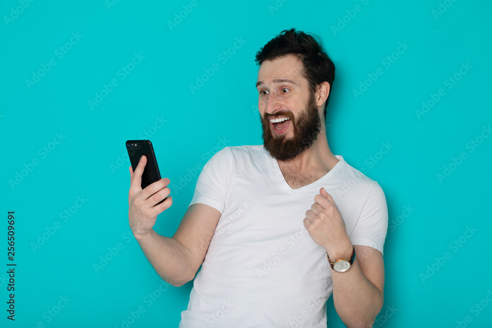 Portrait of an excited man standing over blue background, holding mobile phone, celebrating Portrait of an excited man standing over blue background, holding mobile phone, celebrating