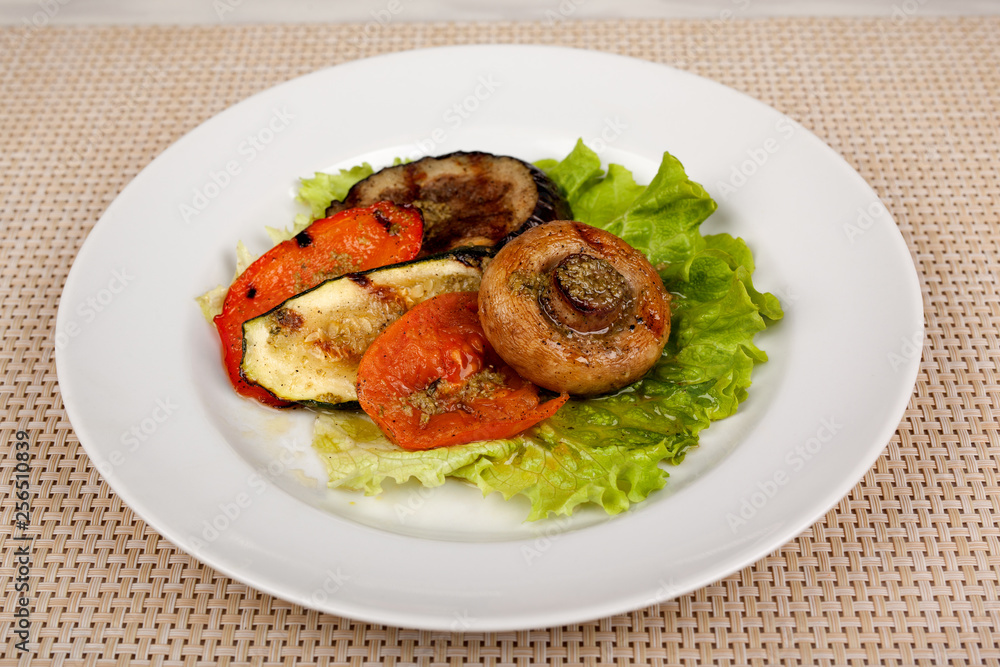Fried mushroom champignon, eggplant, tomato and green leaf lettuce on a white round plate. Fried mushroom champignon, eggplant, tomato and green leaf lettuce on a white round plate.