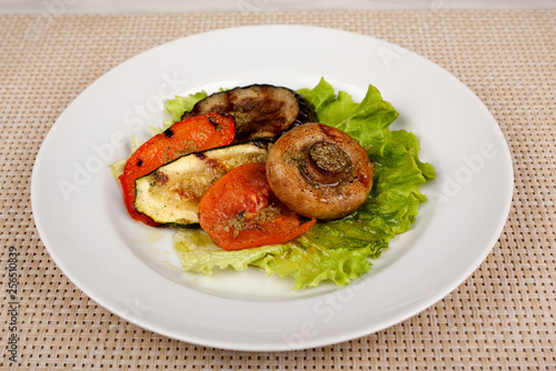 Fried mushroom champignon, eggplant, tomato and green leaf lettuce on a white round plate.