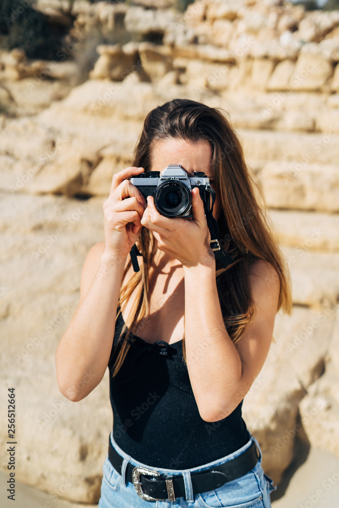 Attractive young woman making photos on her vintage camera on the beach during summer vacation