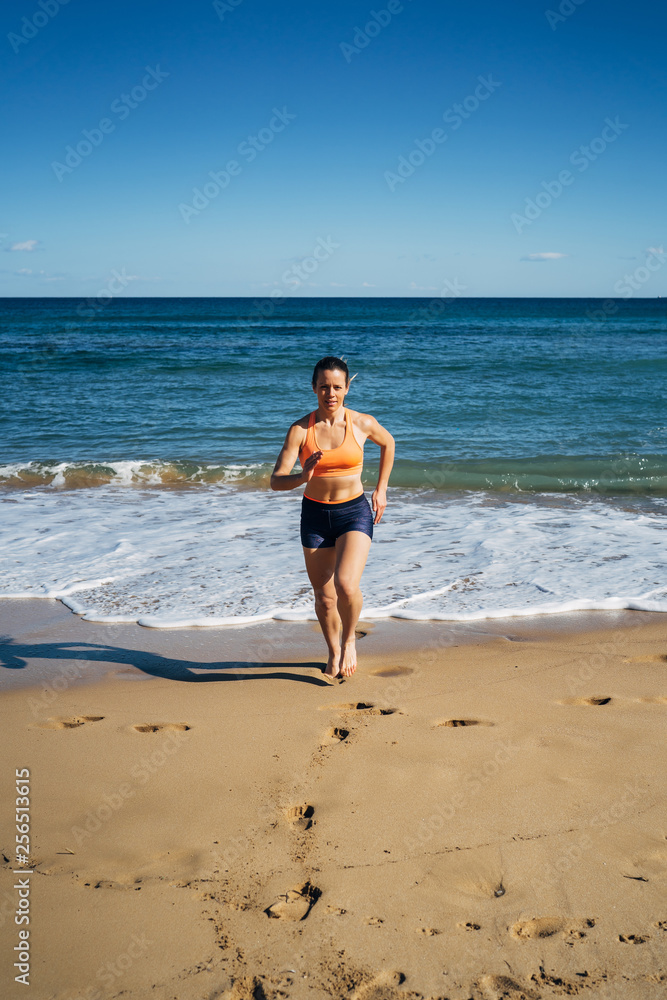 Fitness young woman running on the beach during summer holiday