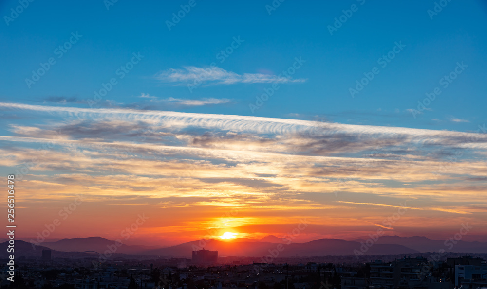 Sunset view Athens, Greece. Sun falling over mountains, blue sky with clouds background