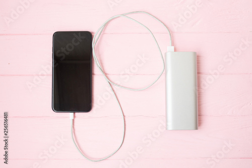 Phone charging with energy bank. Depth of field on Power bank. Pink wooden background.