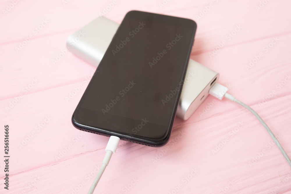 Phone charging with energy bank. Depth of field on Power bank. Pink wooden background. Phone charging with energy bank. Depth of field on Power bank. Pink wooden background.