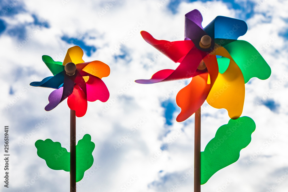 A colored Catherine wheel wind (pinwheel) with wooden stick. Shot from below with blue sky and clouds in the background, on a windy day. A colored Catherine wheel wind (pinwheel) with wooden stick. Shot from below with blue sky and clouds in the background, on a windy day.