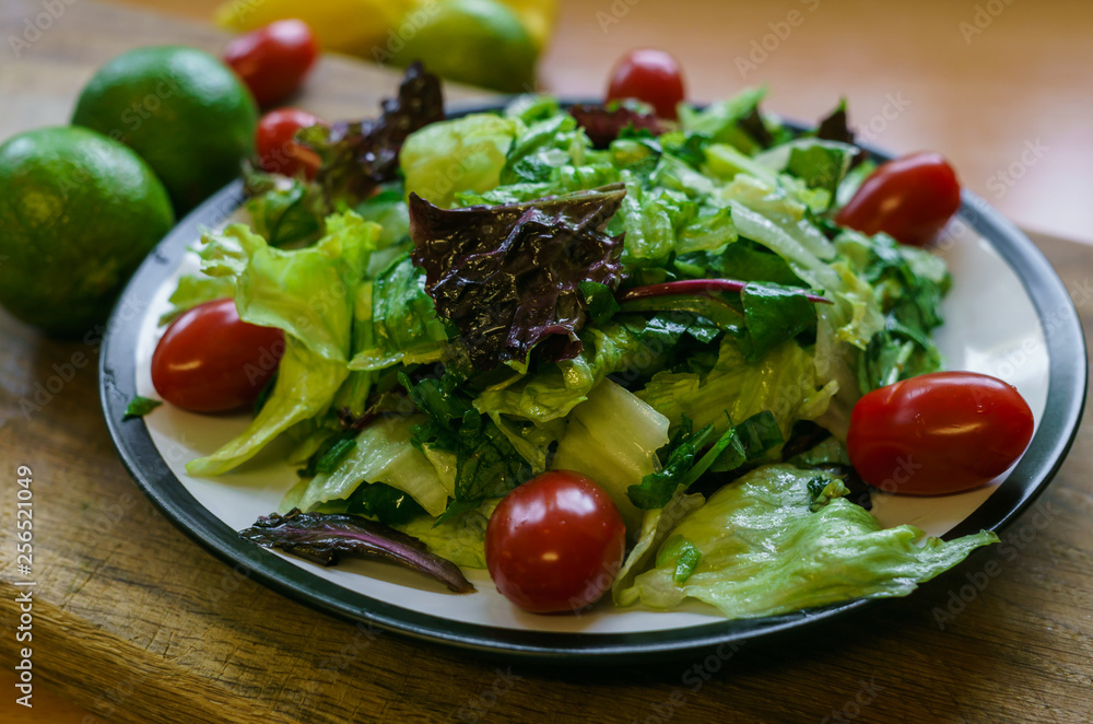 Fresh salad from different types of greens and cherry tomatoes, seasoned with olive oil and lime juice with lemon.