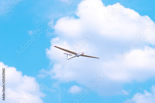 Small glider flying against the blue sky and clouds