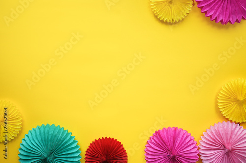 Different paper flowers on yellow table top view. Festive or party background. Flat lay style. Copy space for text. Birthday greeting card.