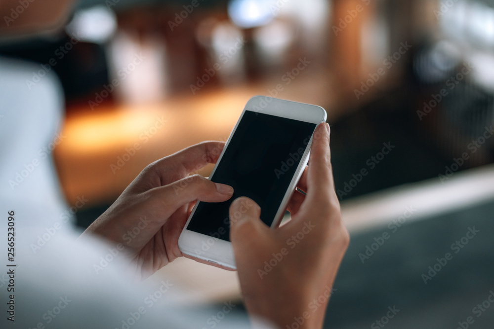 Woman using a smartphone read and text messages with blank space screen display from behind view- woman office worker- digital and communication concept Woman using a smartphone read and text messages with blank space screen display from behind view- woman office worker- digital and communication concept