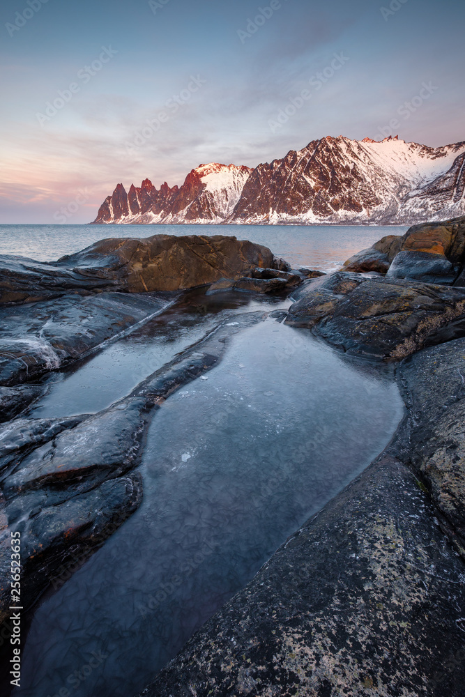 Frozen Rockpool in front of snowy mountains and sea, Oksen Tungeneset Senja, Norway