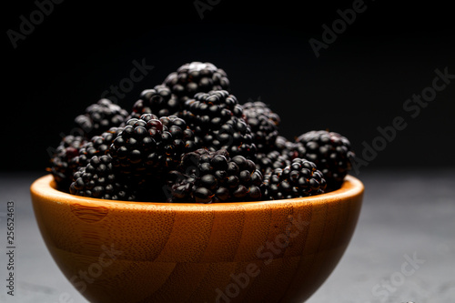 Photo of blackberry in wooden cup on empty black background.