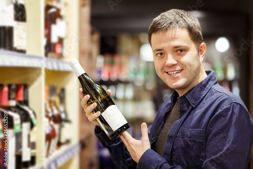 Photo of man with bottle of wine near shelves with bottles