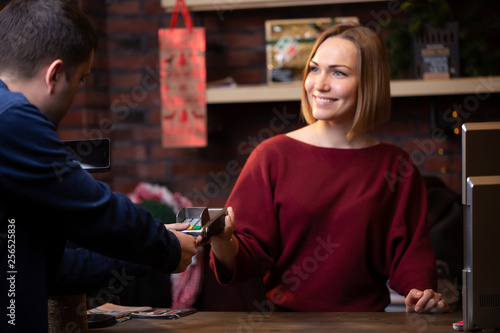 Photo of smiling seller woman standing behind cash register and male buyer from back