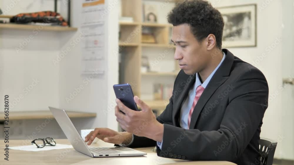 African Businessman Using Phone and Laptop for information African Businessman Using Phone and Laptop for information