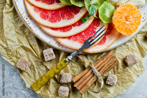 Assorted fruit on a plate, restaurant. Grapefruit, tangerine, kiwi, orange, banana, Apple. Grey background, top view, close up