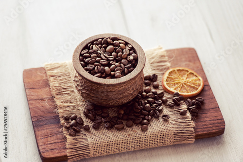 Closeup of coffee beans in wooden rustic bowl on bright background decorated with orange slice.