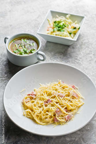 Three dishes in the restaurant, Pasta Carbonara, green salad and chicken soup. Gray background, top view