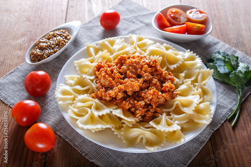 Farfalle bolognese pasta with minced meat on brown wooden background.