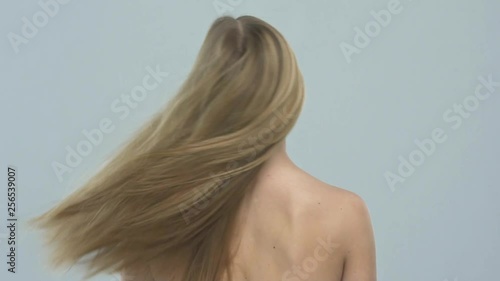 Beautiful blond woman with long hair. Woman with straight hair, posing at studio. Slow motion. Rear view