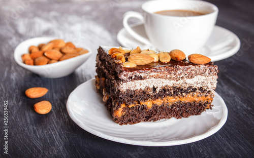 Chocolate cake with caramel, peanuts and almonds on a black wooden background.