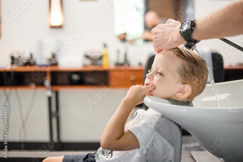 Hairdresser washes the hair of a blond child in a barbershop