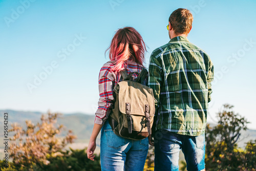 Back view of a couple of young happy backpackers standing at the mountain top enjoying scenery