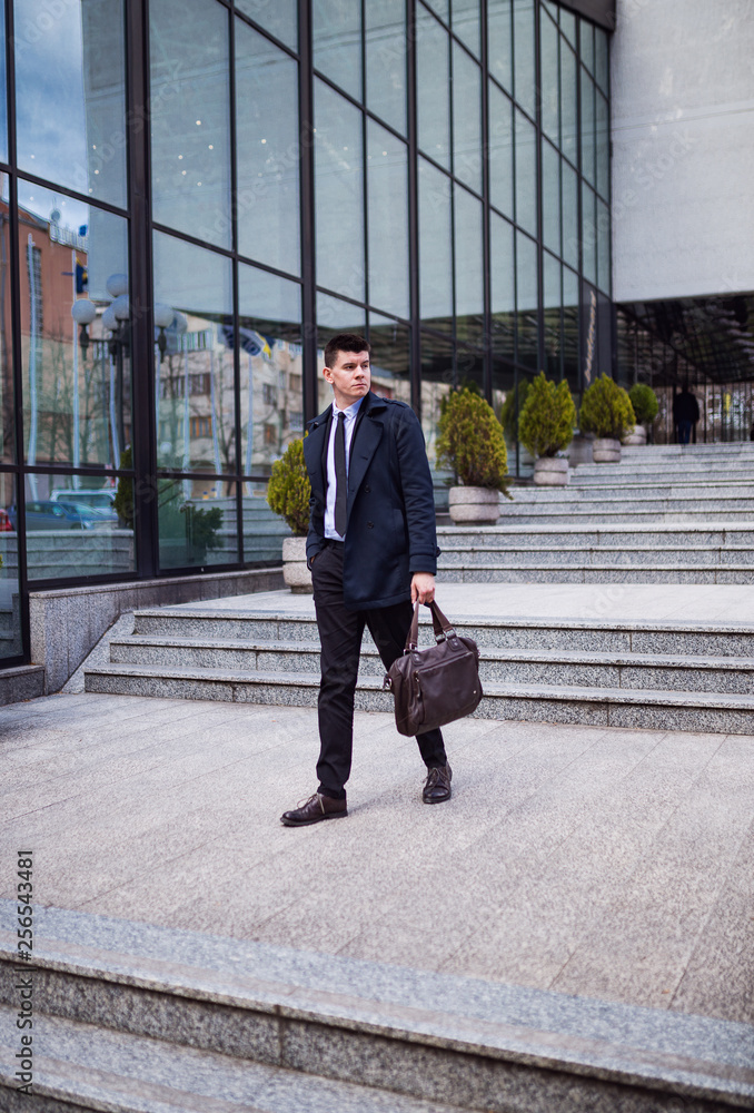 Young Businessman holding briefcase in hand and walking in city