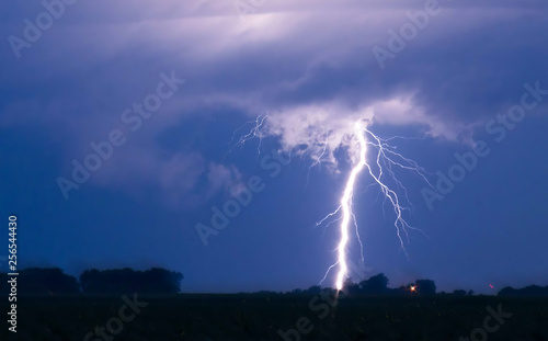 Stormy night single large lightning bolt with multiple branches, silouhetted foreground, and swirling storm clouds