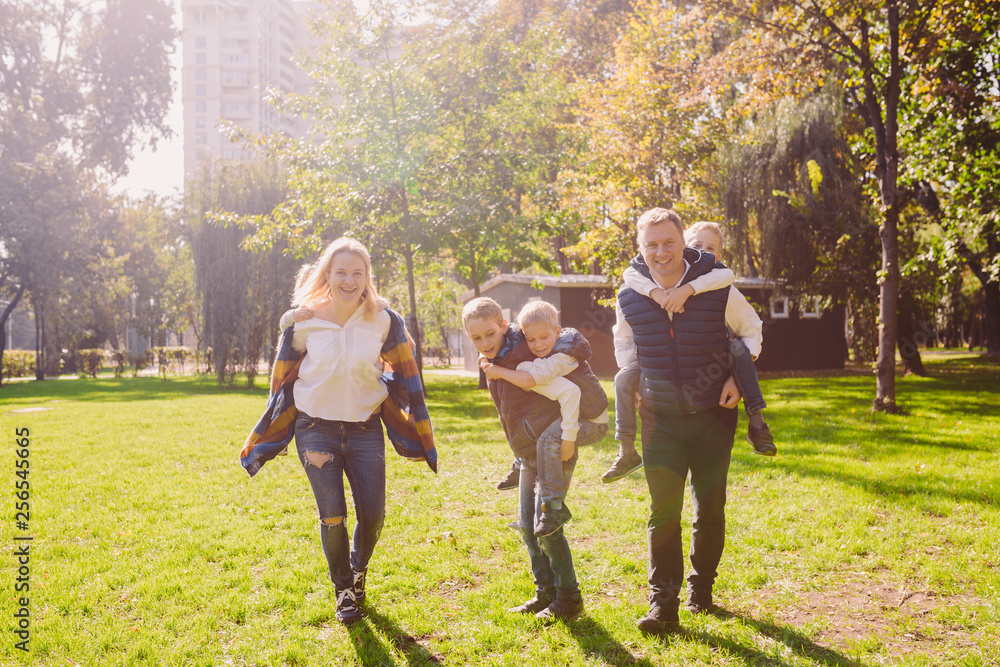 Fototapeta premium Theme family active leisure outside in nature. large Caucasian family with four children. Mom and Dad actively relaxing. enjoy life in park near house on grass. Children on back shoulders roll on top