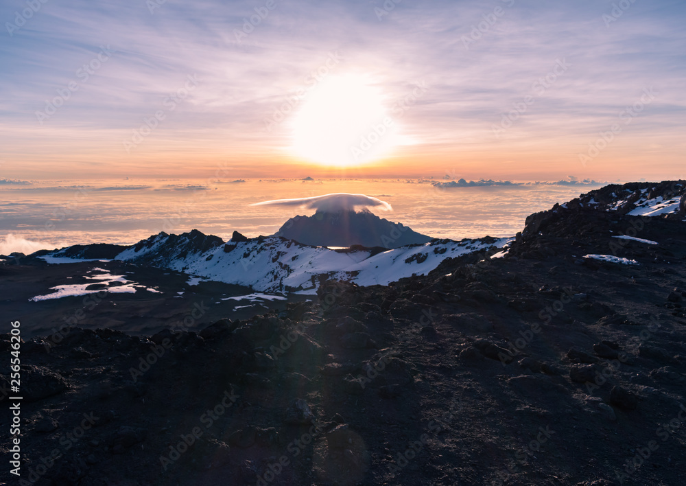 Stunning sunrise view of Mawenzi Peak across the crater at the summit of Kilimanjaro taken from Uhuru Peak. Behind Stella point, Mawenzi sits above the clouds, with a lenticular cloud hanging on top