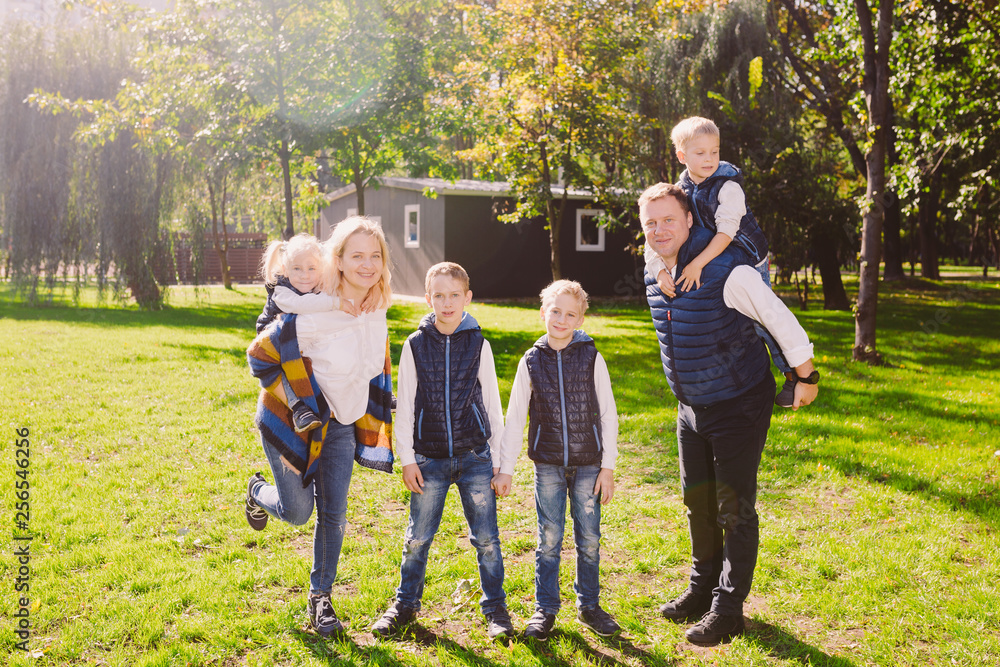 Fototapeta premium Theme family active leisure outside in nature. large Caucasian family with four children. Mom and Dad actively relaxing. enjoy life in park near house on grass. Children on back shoulders roll on top