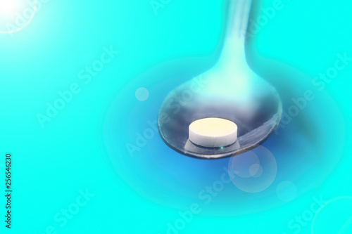 Metal spoon with white pills on blue background  patient treatment concept