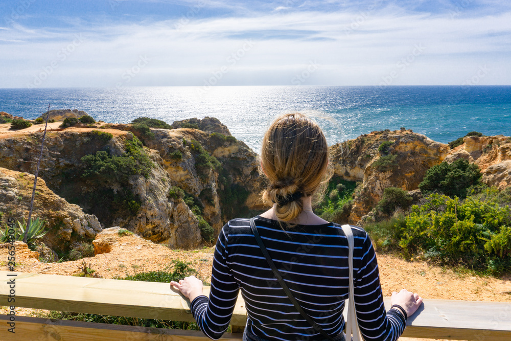 Young blonde haired woman looks out over beautiful ocean scene in Portugal