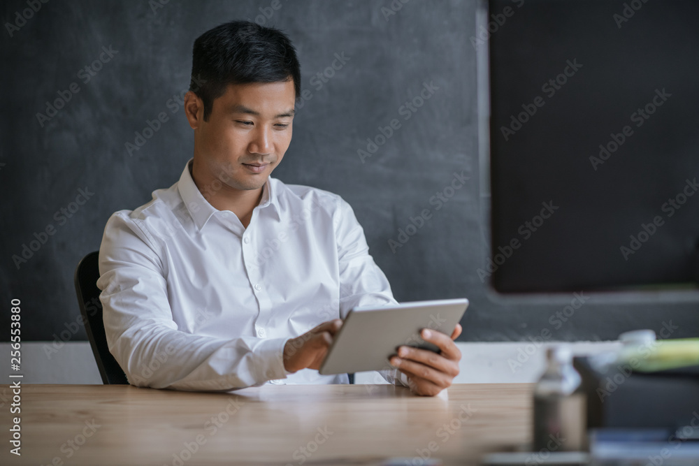 Smiling Asian businessman working on a tablet in an office Smiling Asian businessman working on a tablet in an office