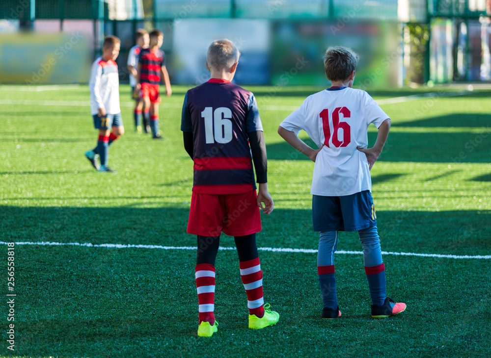 Obraz premium Boys in red white sportswear running on soccer field. Young footballers dribble and kick football ball in game. Training, active lifestyle, sport, children activity concept 