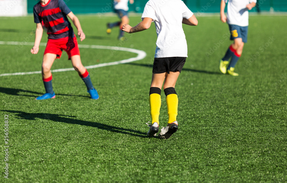 Boys in red white sportswear running on soccer field. Young footballers dribble and kick football ball in game. Training, active lifestyle, sport, children activity concept 