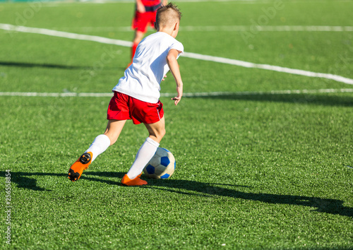 Boys in red white sportswear running on soccer field. Young footballers dribble and kick football ball in game. Training, active lifestyle, sport, children activity concept  © Natali