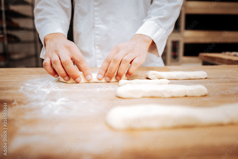 Young baker wearing white jacket forming baguettes on tray Young baker wearing white jacket forming baguettes on tray