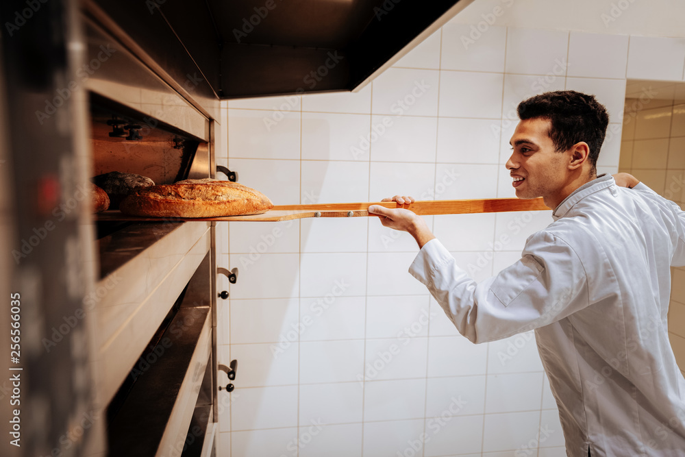 Baker smiling while taking baguettes out of oven Baker smiling while taking baguettes out of oven