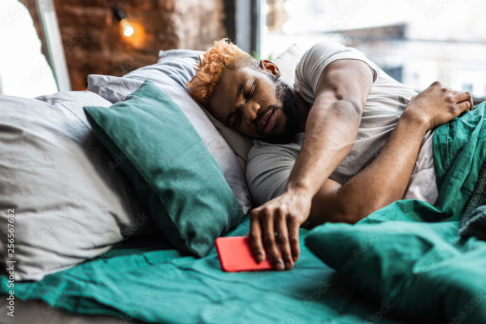 Fototapeta premium Nice sleepy man taking his mobile phone